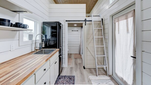 Cocina estrecha con techo de madera, horno empotrado, lavabo y escalera que conduce a una zona de dormir en un altillo.