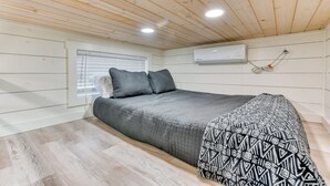 Een slaapkamer met een bed, een raam met zonwering, een airconditioning en een houten plafond.