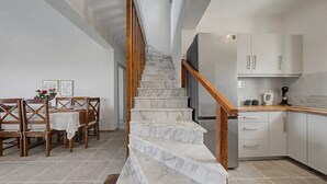 A staircase with marble steps, wooden railings, a dining area with wooden chairs and a table, and a kitchen with white cabinets and appliances.