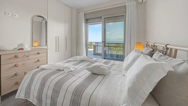 A bedroom with a bed, a dresser, a mirror, and a balcony with a view.