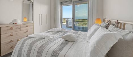 A bedroom with a bed, a dresser, a mirror, and a balcony with a view.