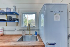 A kitchen with a stainless steel sink, a blue refrigerator, and shelves with dishes and cups. - Santorini-Style Tiny Home | Cobalt Blues, Fire Pit & Hill Country Stars (Blanco)