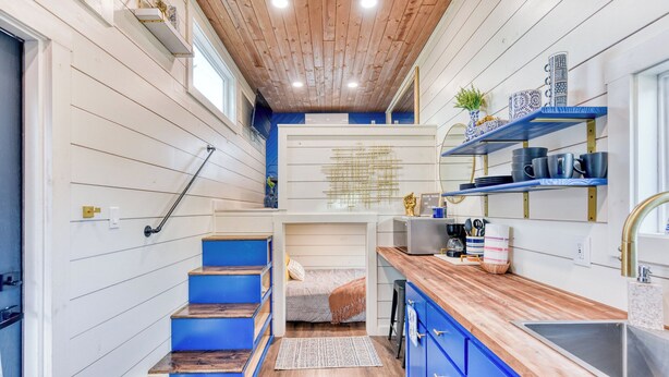 Eine kleine Küche mit blauen Schränken, einer Holz Arbeitsplatte und einem eingebauten Regal mit Küchenutensilien.