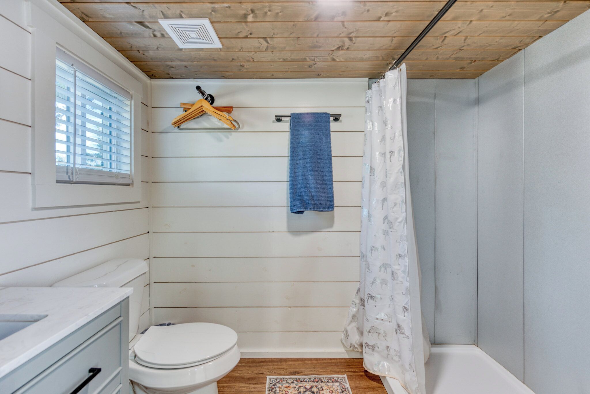 Un bagno piccolo e compatto con soffitto in legno, un water bianco, una doccia con tenda decorata e un asciugamano su un portascopevoli.