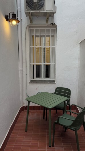 Un pequeño espacio al aire libre con una mesa y sillas, una ventana con rejas y un equipo de aire acondicionado instalado en la pared.