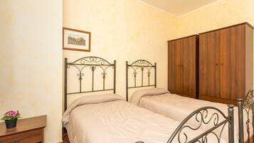 Une chambre avec deux lits, une armoire en bois, une table de chevet avec une plante et un tableau encadré au mur.