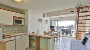 A compact kitchen with a dining area, a small refrigerator, a microwave, and a window overlooking a balcony. - Capitainerie – Marina des Sables d’Olonne (Les Sables-d´Olonne)