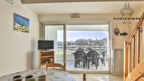 A dining area with a table set for two, a television, and a view of the city through a sliding glass door. - Capitainerie – Marina des Sables d’Olonne (Les Sables-d´Olonne)