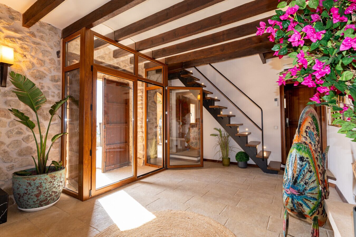 Ein geräumiger Innenraum mit Steinwand, Holzbalken, einer Treppe und einer großen Kübelpflanze.