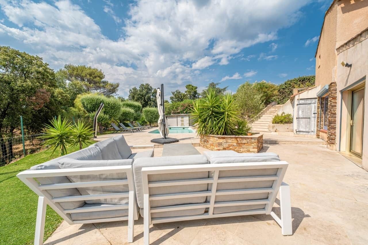 Eine Terrasse mit zwei weißen Liegestühlen, einem Pool und einer Steinmauer mit Pflanzen.