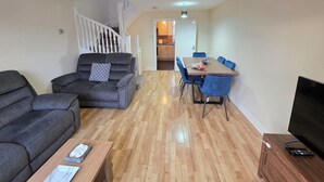 Ein Wohnzimmer mit einer Couch, einem Esstisch mit Stühlen, einem Fernseher und einer Treppe, die in einen anderen Raum führt.