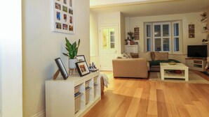 A living room with a sofa, coffee table, and TV. There is a plant on a stand, a white cabinet with shelves, and a door with glass panels. - Gordon Avenue (Camberley)