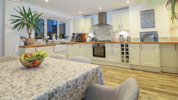 A modern kitchen with white cabinets, a central island, and a dining area with a table set for two. - Gordon Avenue (Camberley)