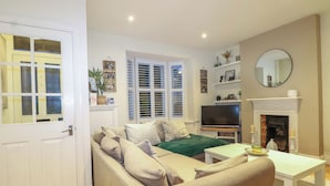 A living room with a beige sofa, a white coffee table, a flat-screen TV, and a fireplace. - Gordon Avenue (Camberley)