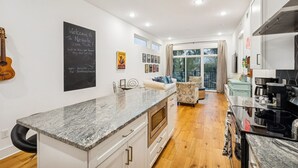 Eine moderne Küche mit Granit Arbeitsplatte, weißen Schränken und einem eingebauten Ofen. Es gibt eine Sitzecke mit Sofa und Sesseln, und ein großes Fenster sorgt für natürliches Licht.