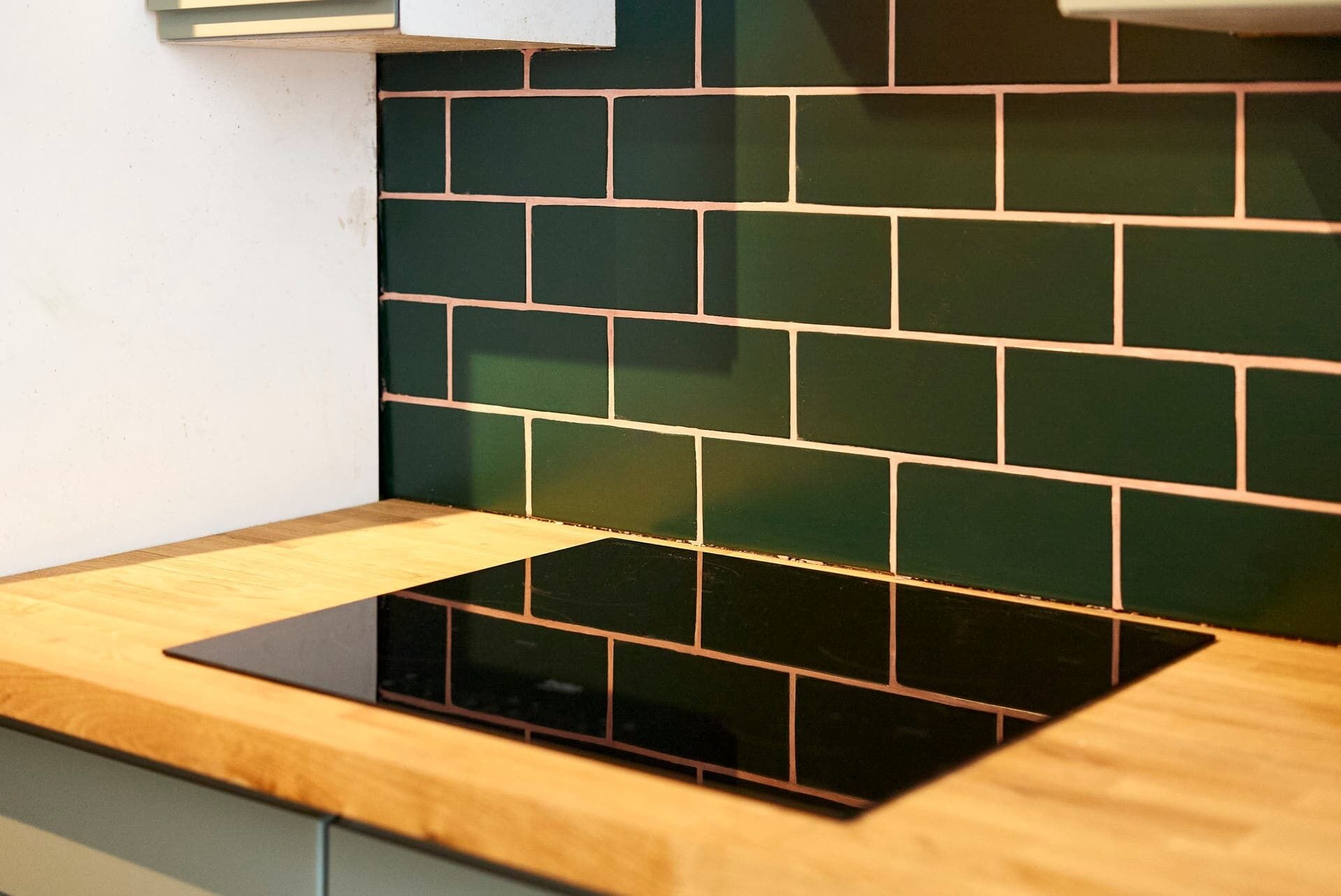 A kitchen with a black induction cooktop and green backsplash tiles.