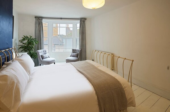 Une chambre à coucher avec un grand lit, deux fauteuils, un radiateur et une fenêtre avec des rideaux.