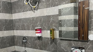 Een moderne badkamer met een marmeren betegelde muur, een witte wastafel en een douchehoek.