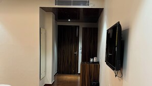 Een moderne hotelkamer met een houten vloer, een bed, een aan de muur bevestigde televisie en een klein kitchenette-gedeelte.