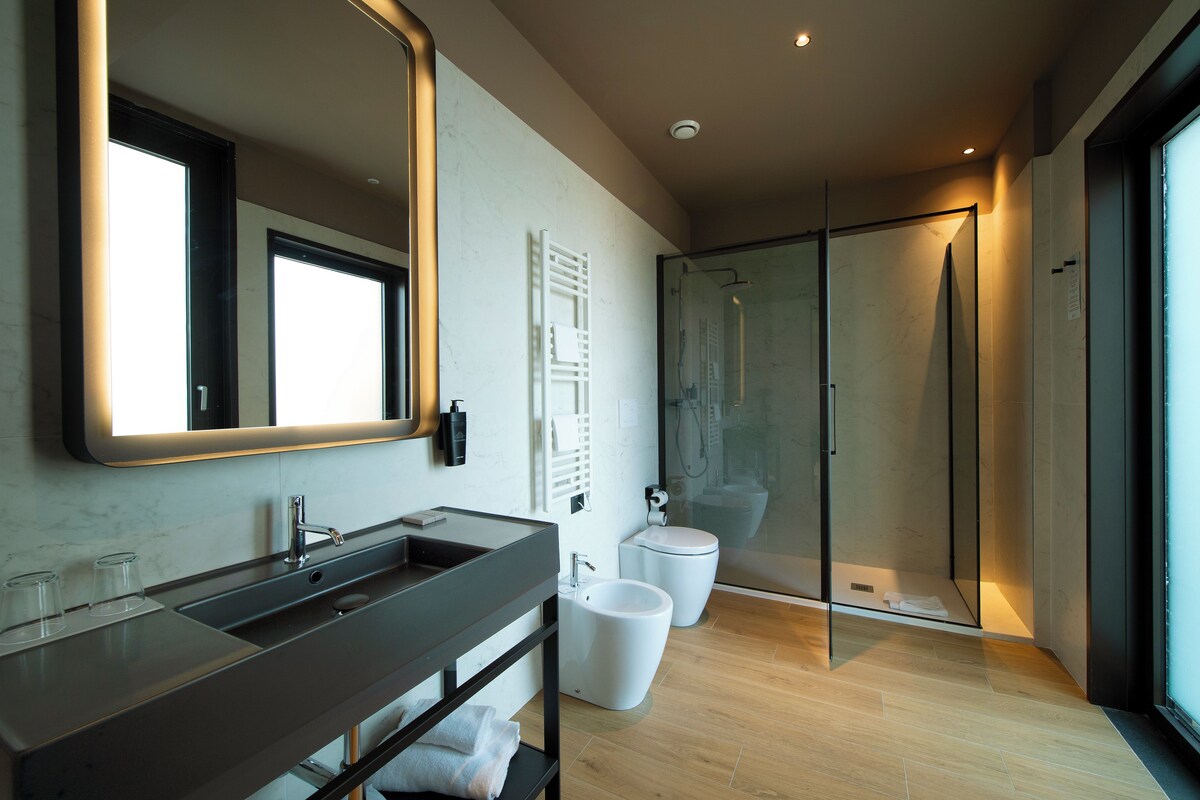 Un baño moderno con un espejo grande, un lavabo, un bidé y una ducha con mampara de vidrio.