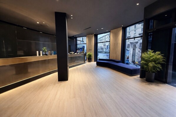 A modern reception area with a wooden floor, black reception desk, and large windows offering views of the city.