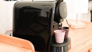 Una cafetera sobre una encimera de madera, con un porta tazas y una lámpara al fondo.