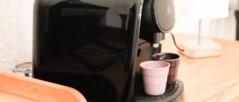 A coffee maker on a wooden counter with a cup holder and a lamp in the background.