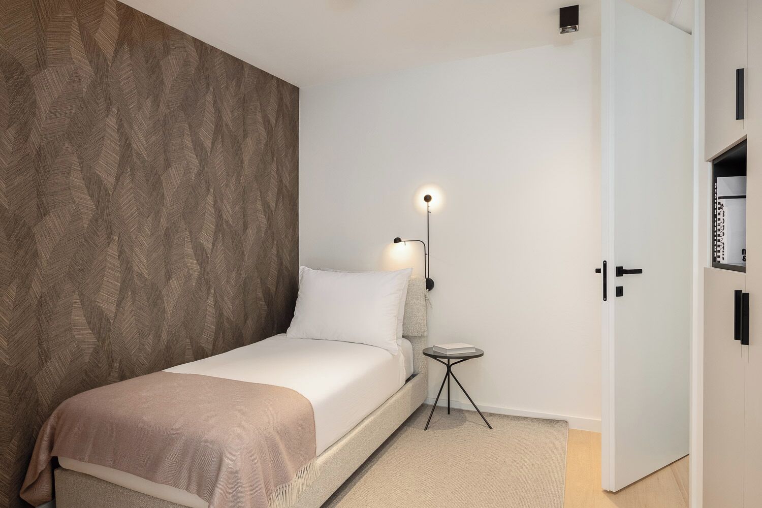 A single bed with a headboard, a bedside table with a lamp, and a wardrobe with a mirror.