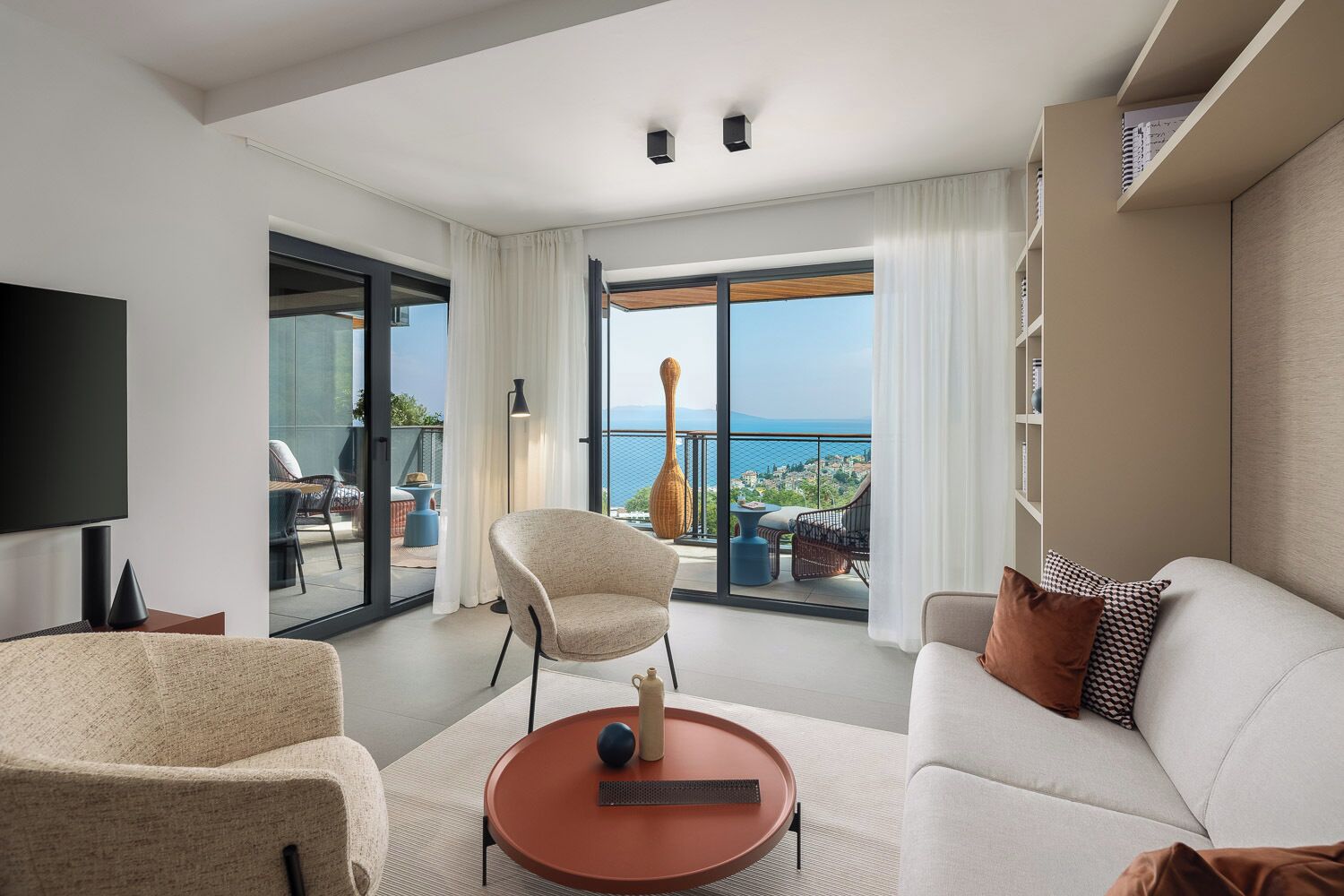 Una habitación de hotel moderna con balcón, un televisor de pantalla plana, un sofá, una silla y una mesa de centro.