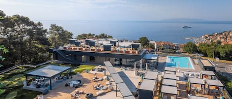 A modern rooftop with a swimming pool, outdoor seating, and a view of the sea.