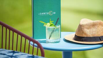 Ein Tisch mit einem Buch mit dem Titel 'CantuCio' und einem Strohhut, vor einem unscharfen grünen Hintergrund.