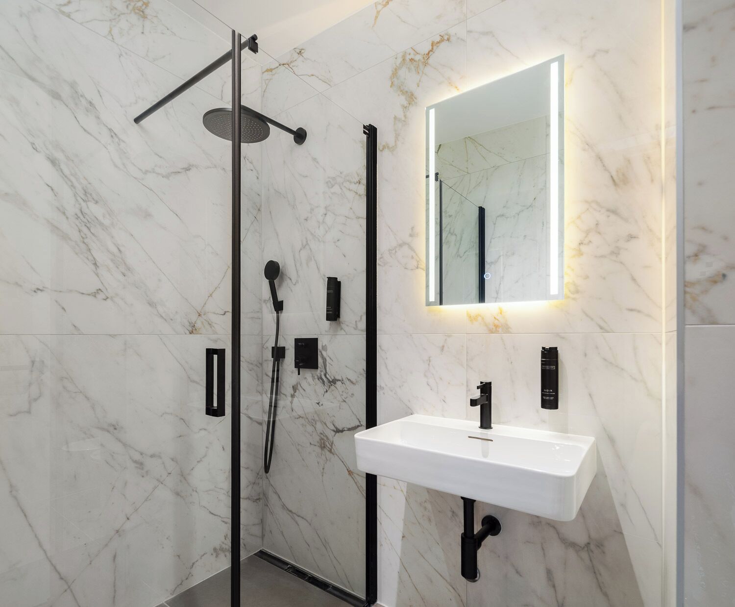 A modern bathroom with a glass-enclosed shower, a white sink, and a mirror with integrated lighting.