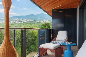 Un balcón con mobiliario de mimbre, una mesa azul y vistas a un pueblo y montañas.