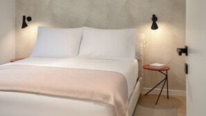 A neatly made bed with a white comforter and pillows, a small bedside table with a book, and a wall with a leaf pattern. - Aminess Younique Vollo Hotel Residences (Opatija)