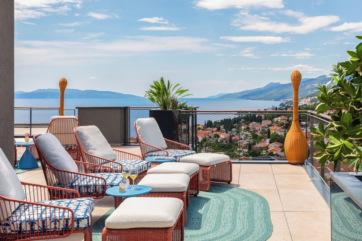 A terrace with wicker furniture, a view of a lake, and a cityscape in the background.