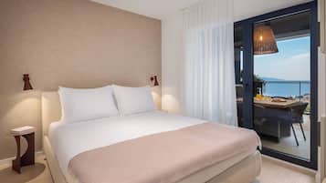 Een hotelkamer met een bed, een nachtkastje, een lamp, uitzicht op de natuur door een glazen deur, en een tafel met stoelen buiten.