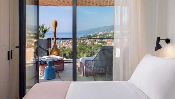 A hotel room with a large bed, a view of the city, and a balcony with outdoor furniture. - Aminess Younique Vollo Hotel Residences (Opatija)