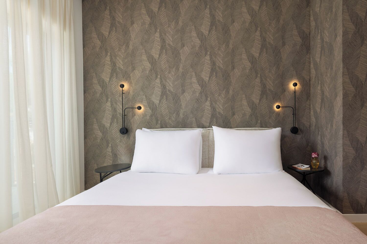 Una camera d'albergo con un letto, due comodini e illuminazione a parete.