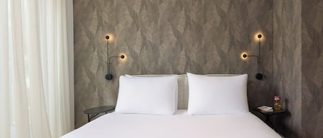A hotel room with a bed, two bedside tables, and wall-mounted lighting.