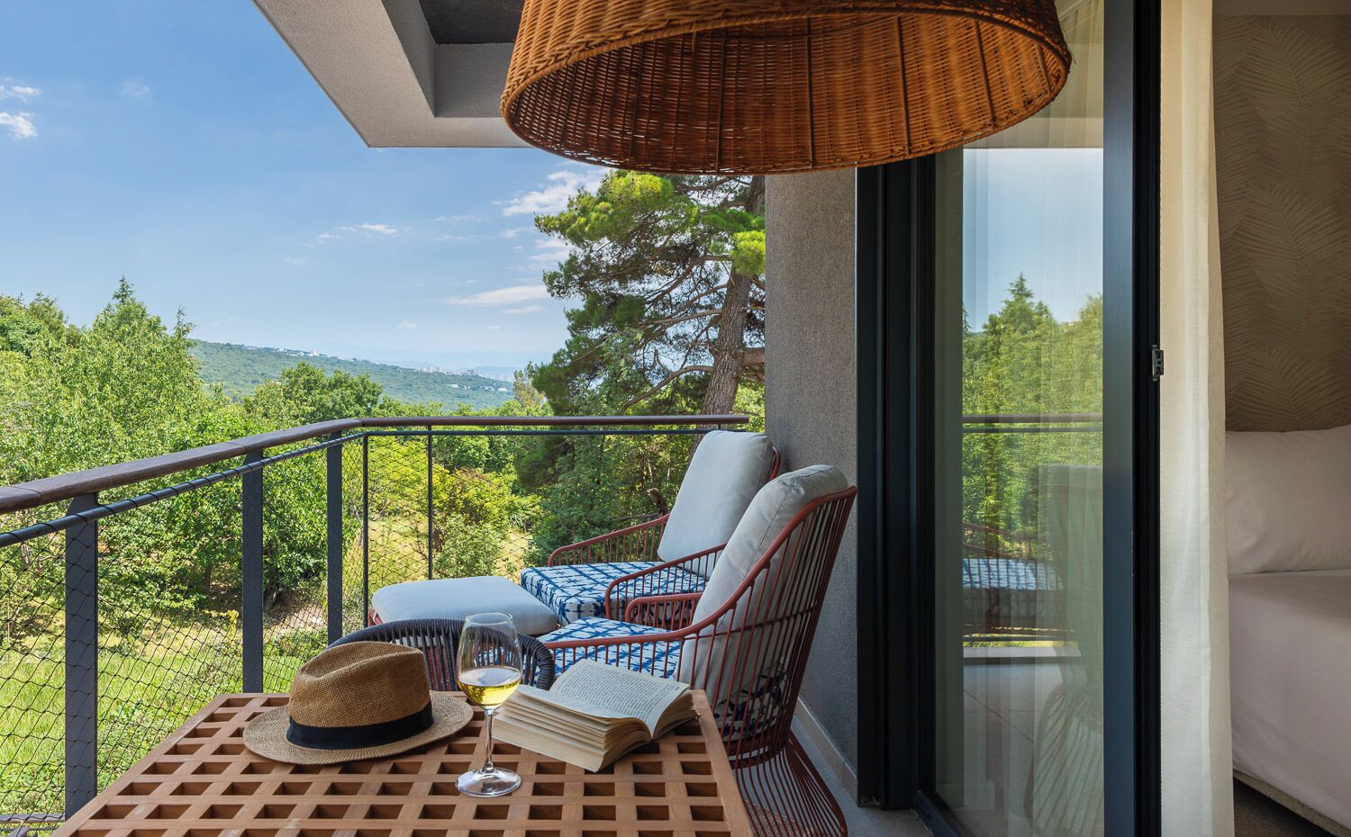 A balcony with wicker furniture, a hat, and a glass of wine.