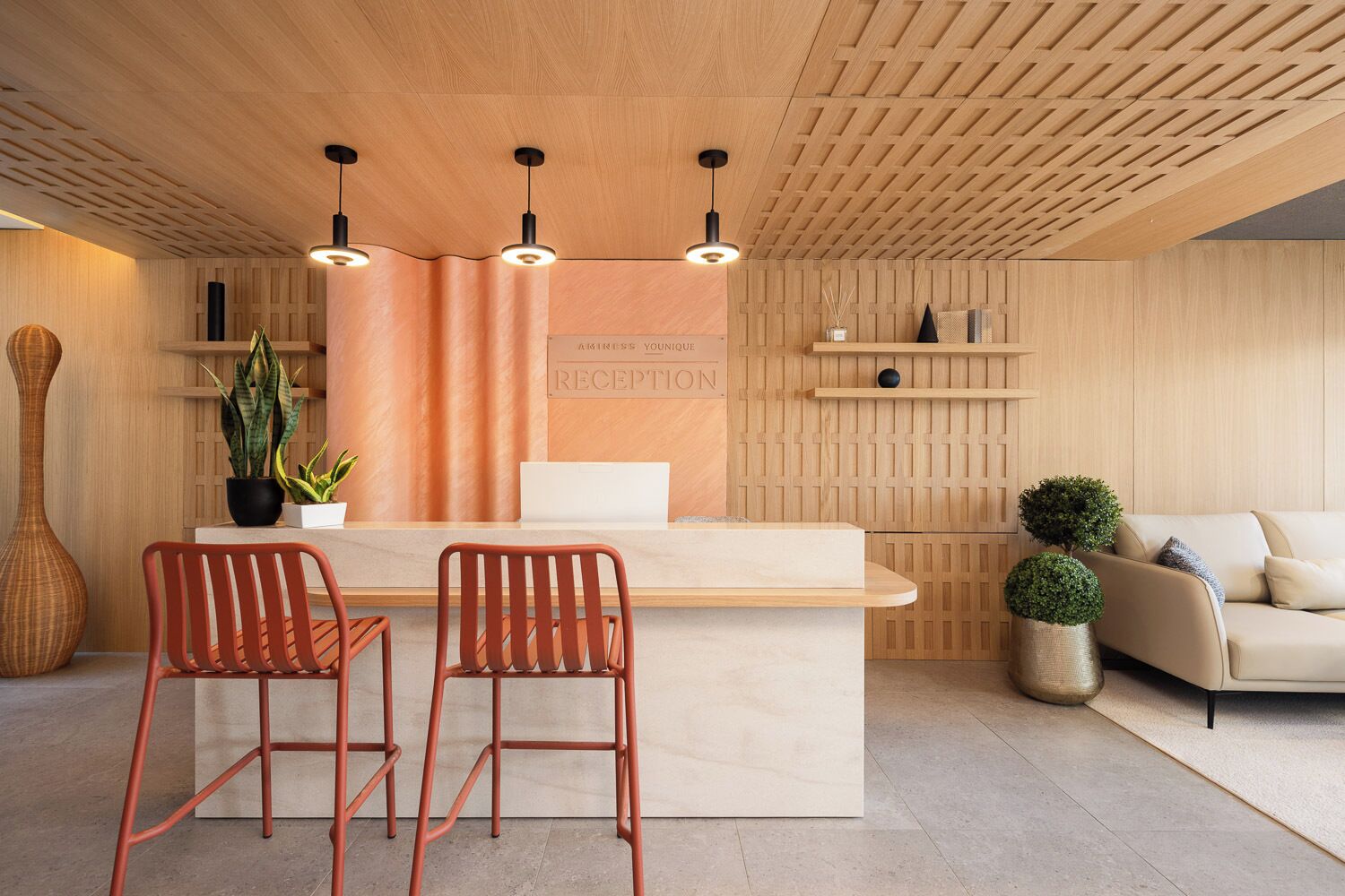 Un área de recepción con un mostrador de madera, dos sillones rojos, un sofá y una planta en maceta.