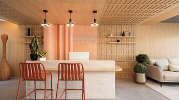 Un área de recepción con un mostrador de madera, dos sillones rojos, un sofá y una planta en maceta.