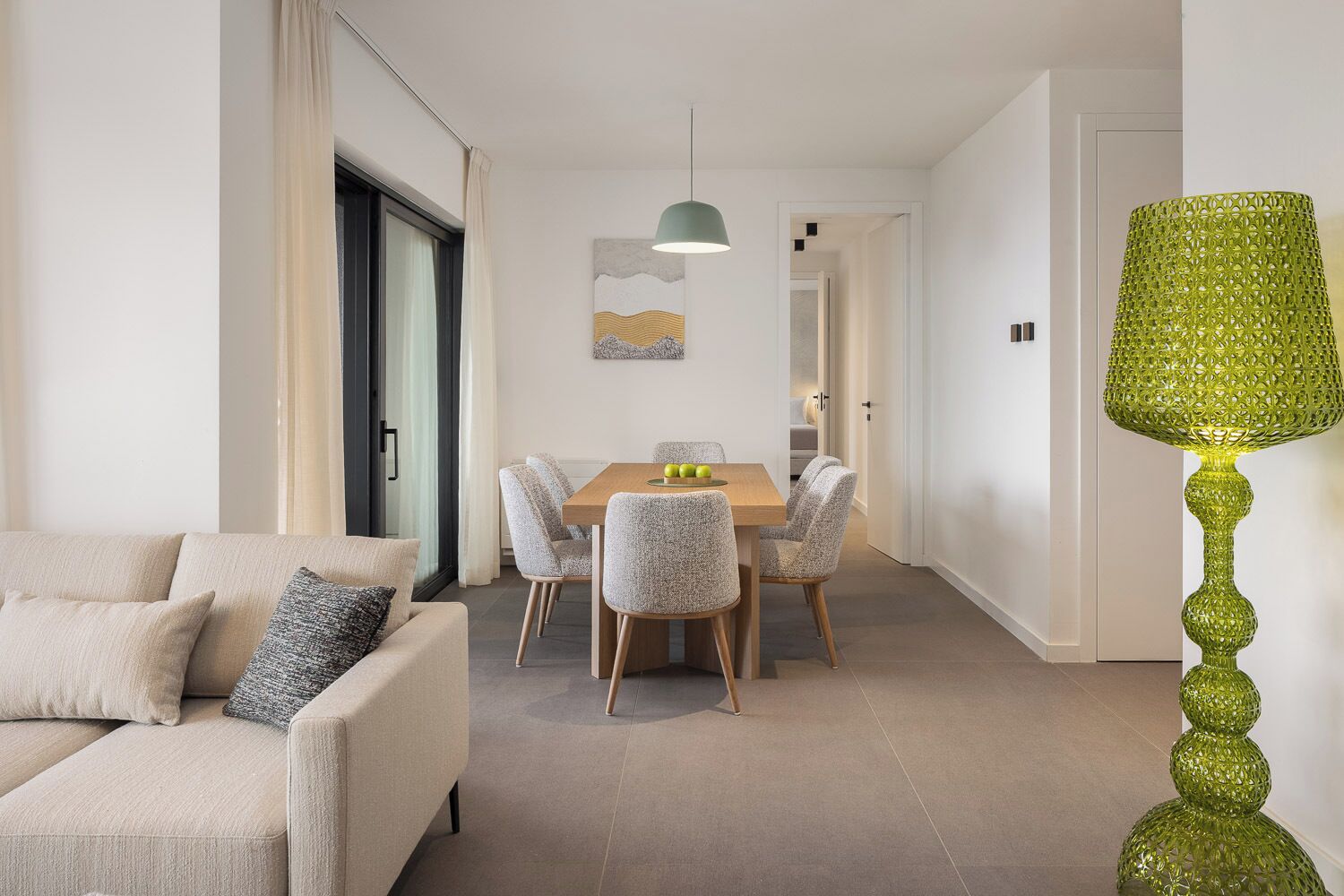 A modern living room with a sofa, a dining area with a table and chairs, and a green decorative lamp.