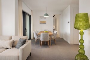 A modern living room with a sofa, a dining area with a table and chairs, and a green decorative lamp.