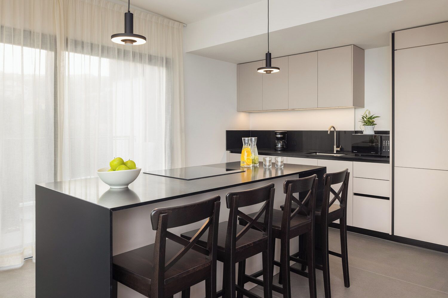A modern kitchen with a central island, black bar stools, a bowl of fruit, and a coffee maker.