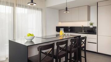 A modern kitchen with a central island, black bar stools, a bowl of fruit, and a coffee maker.