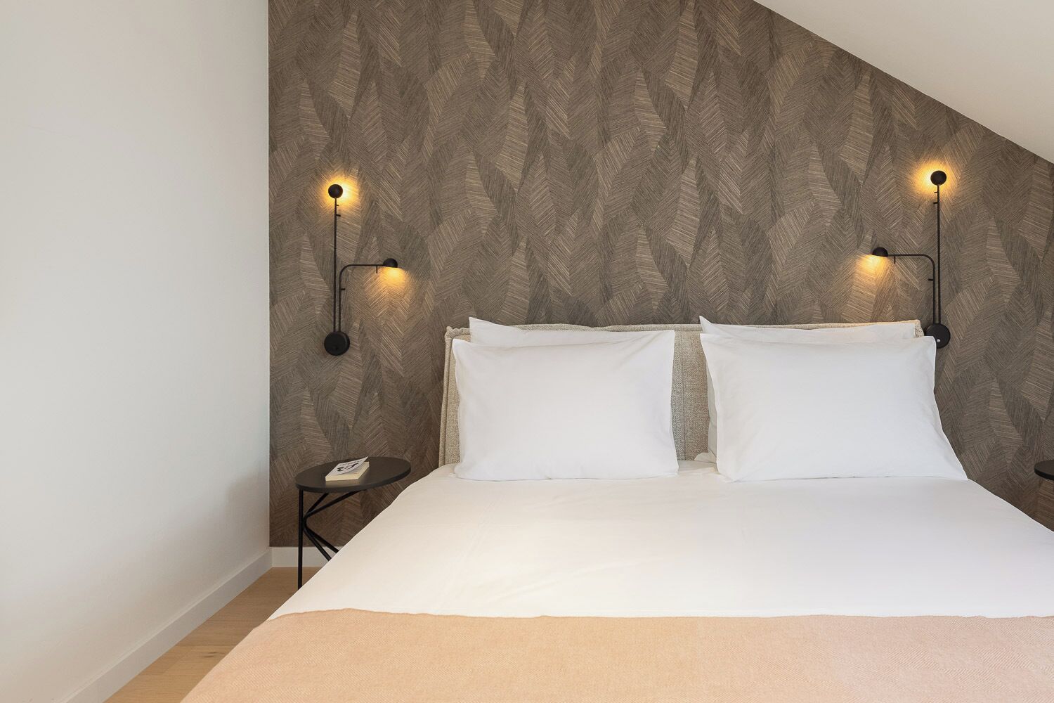 A bedroom with a bed, two bedside tables, and wall-mounted lighting.