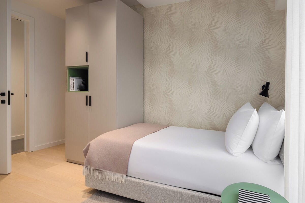 Un dormitorio con cama, armario, estante con libros y pared con diseño de hojas.