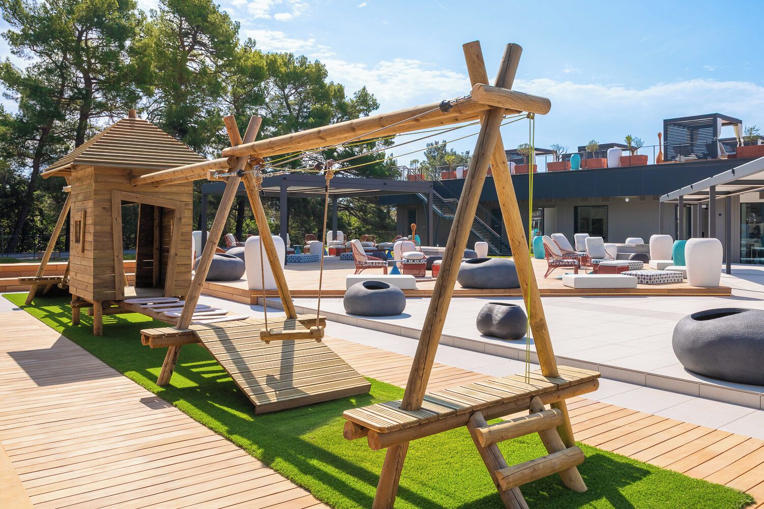 Un conjunto de columpios de madera, una zona de estar al aire libre y una pequeña construcción de madera.