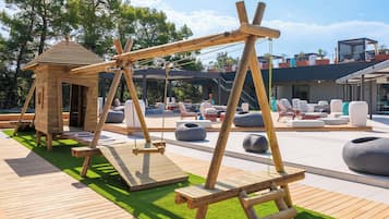 Un conjunto de columpios de madera, una zona de estar al aire libre y una pequeña construcción de madera.